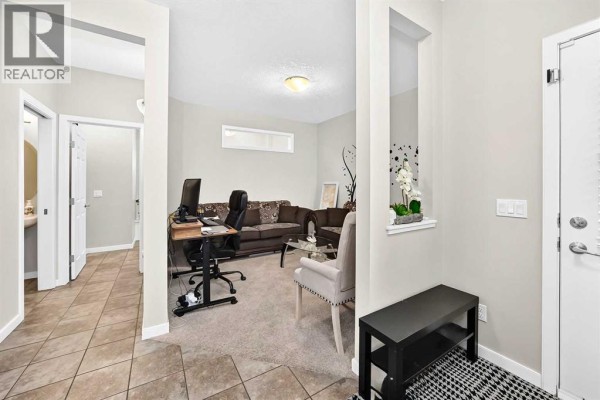 The main floor living area with a sofa, desk, and chairs, viewed from the foyer. - 56 Panatella Parade Nw, Calgary