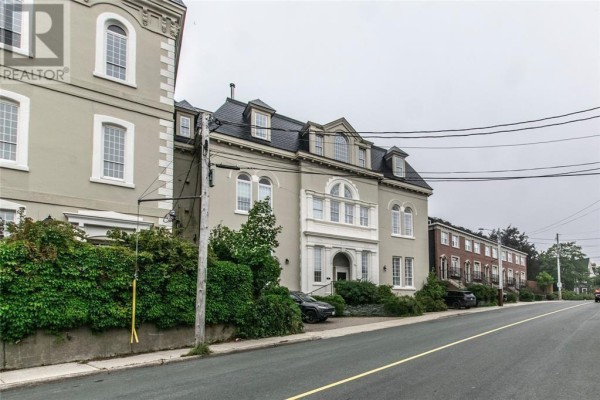 Street view of beige and red brick buildings on a cloudy day with power lines overhead. - 56 Queens Road, St  John S