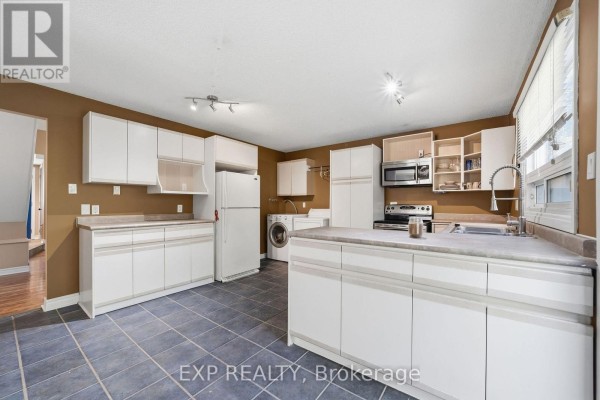 Kitchen with white cabinets, stainless steel appliances including a stove, refrigerator, and dishwasher, and dark tile flooring. - 56 Yardley Place, London North