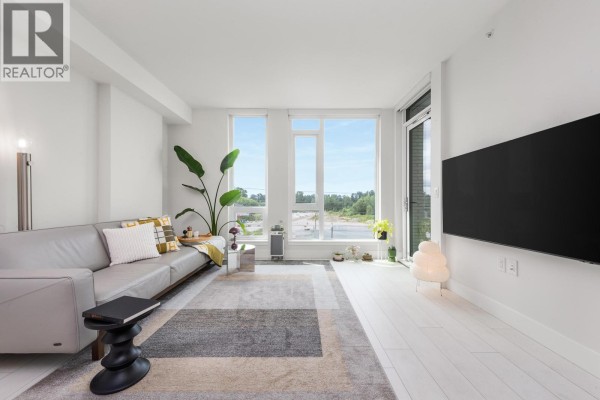 Bright living area with a leather sofa, large windows, and a mounted television. - 560 8575 Rivergrass Drive, Vancouver