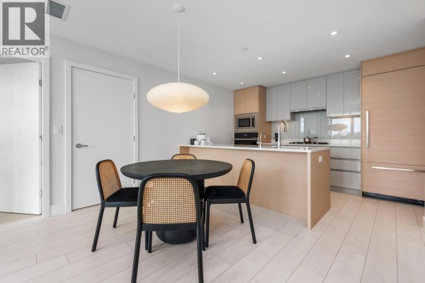 Modern kitchen and dining area with light wood cabinets, an island, and cane-backed chairs. - 560 8575 Rivergrass Drive, Vancouver