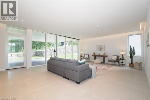 Spacious living room with a gray sectional sofa, large windows, and a stone wall outside. - 560 Werni Court, Waterloo