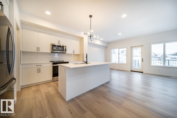 Open concept living area with white kitchen, island, dining area, and large windows. - 5601 69 St, Beaumont