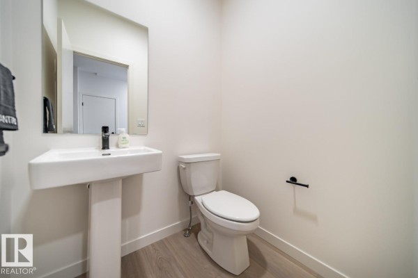 Powder room with white pedestal sink, toilet, and light wood laminate flooring. - 5601 69 St, Beaumont