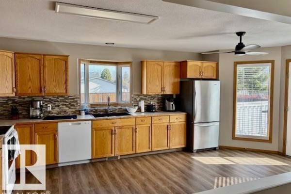 Oak kitchen cabinets with mosaic tile backsplash, white appliances, and bay window. - 5609 45a St, Vegreville