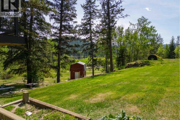 Wooden deck with railing and outdoor furniture overlooks a forested valley with distant homes. - 5612 Canim-hendrix Lake Road, 100 Mile House