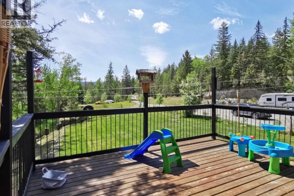 Wooden deck with railing, children's toys, and BBQ grill with views of trees and sky. - 5612 Canim-hendrix Lake Road, 100 Mile House