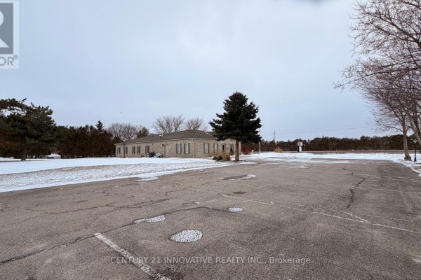 Exterior view of a light brick commercial building with a large asphalt parking lot. - 5615 Mcgillivray Drive N, Lucan Biddulph
