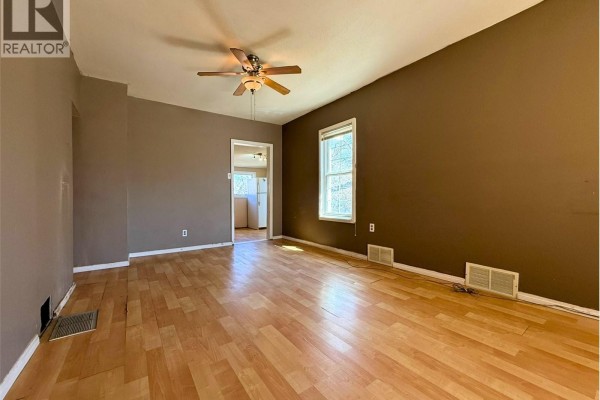 Living room with brown walls, light wood laminate flooring, and a view into the adjacent kitchen area. - 562 Athabasca Street W, Moose Jaw