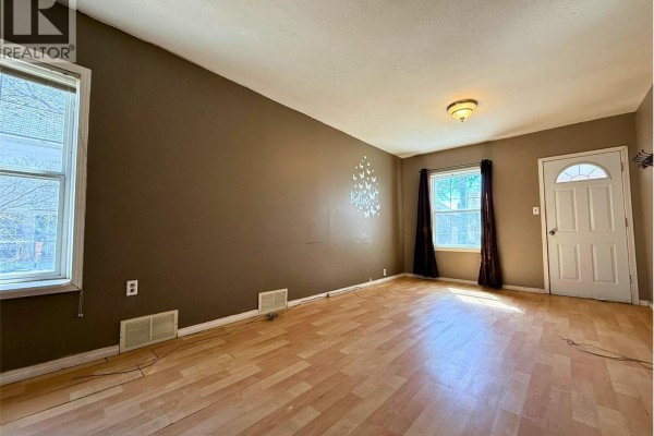 Living room with brown walls, light wood laminate flooring, a window, and a white door. - 562 Athabasca Street W, Moose Jaw