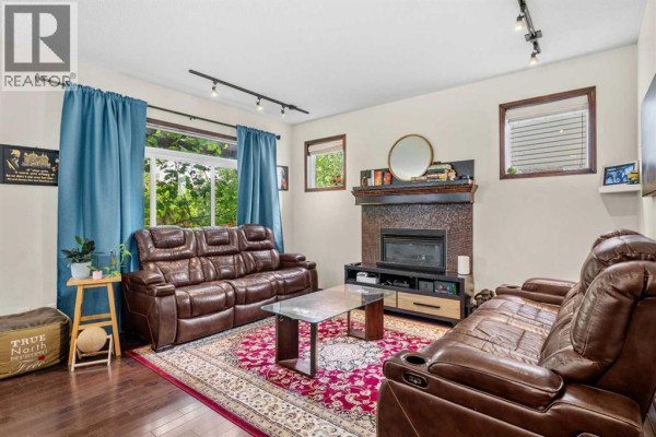 Living room featuring brown leather couches, a fireplace with dark tile surround, and blue curtains. - 562 Cranston Drive Se, Calgary