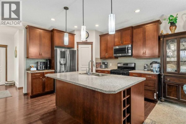Kitchen with dark wood cabinets, granite countertops, stainless steel appliances, and a large island. - 562 Cranston Drive Se, Calgary
