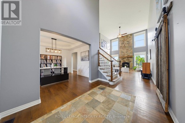 Interior view of a foyer with hardwood floors, leading to a staircase and a living area with a stone fireplace. - 562 Pennycross Lane, Ottawa