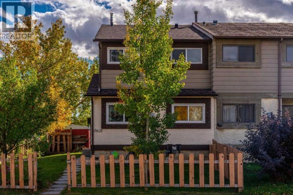 Front exterior of a townhouse with a green lawn and a light brown wooden fence in front. - 5631 1 Avenue Se, Calgary