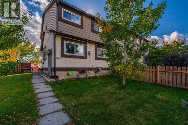 Side view of a townhouse showing a concrete pathway leading to the front door and green grass. - 5631 1 Avenue Se, Calgary