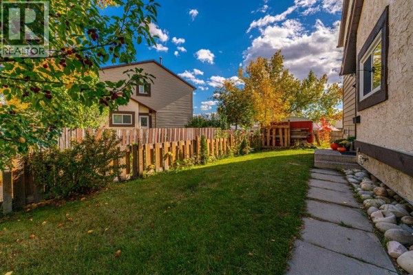 Backyard view of the townhouse property with a large green lawn, a wooden fence, and a stone pathway. - 5631 1 Avenue Se, Calgary