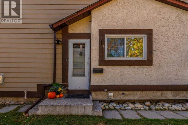 Close-up of the townhouse front entrance with a white door, window, and concrete steps decorated with pumpkins. - 5631 1 Avenue Se, Calgary
