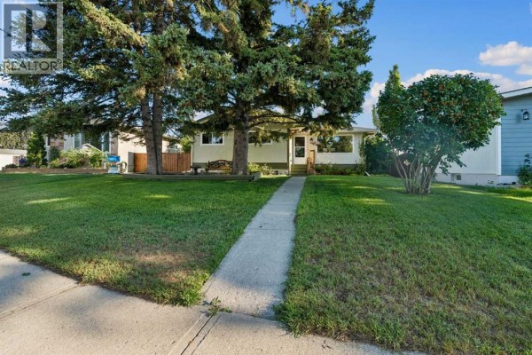 View of the side yard with a wrought-iron bench under a large evergreen tree. - 5635 Travis Crescent Ne, Calgary