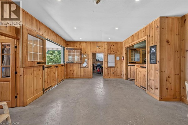 Interior of a barn with wooden walls, multiple stable doors with windows, and concrete flooring. - 564 8th Concession Road E, Carlisle