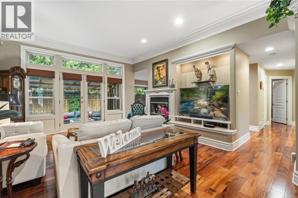 Living room with fireplace, television, and french doors leading to an outdoor patio. - 564 Hazelwood Pl, Qualicum Beach