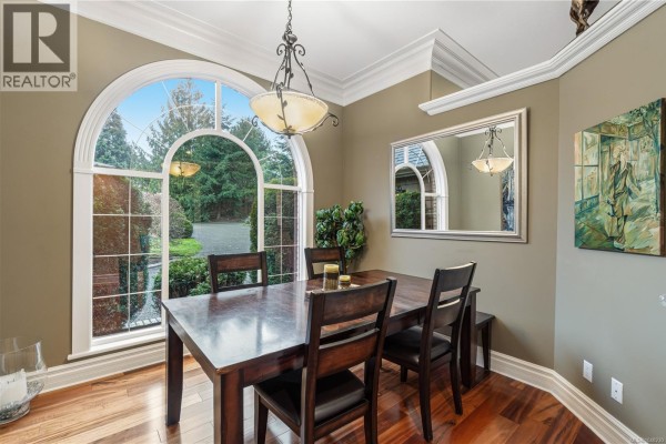 Dining room with a large arched window overlooking the front yard and a wooden dining set. - 564 Hazelwood Pl, Qualicum Beach