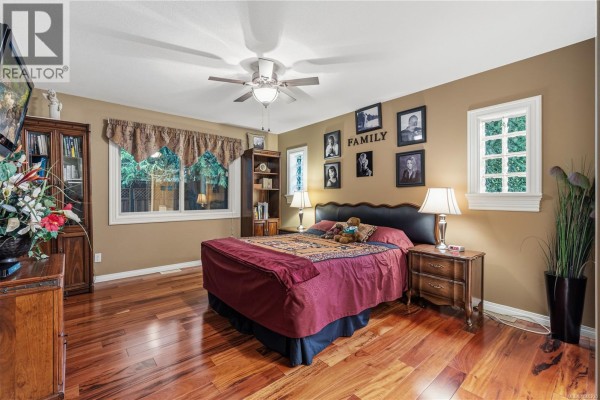 Bedroom with a king-size bed, wooden furniture, and large windows with garden views. - 564 Hazelwood Pl, Qualicum Beach
