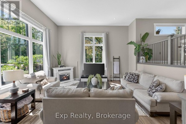 Living room with a fireplace, large windows, neutral-colored sofas, and wood-look flooring. - 564 Sidney Street, Belleville