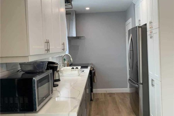 Basement kitchen with white cabinets, white appliances, and a small wooden dining table with two chairs. - 5644 Hanan Avenue, Niagara Falls