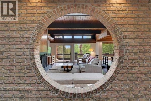 Living room viewed through a circular brick opening, featuring a fireplace, sofa, and large windows. - 565 Fountain Street S, Cambridge