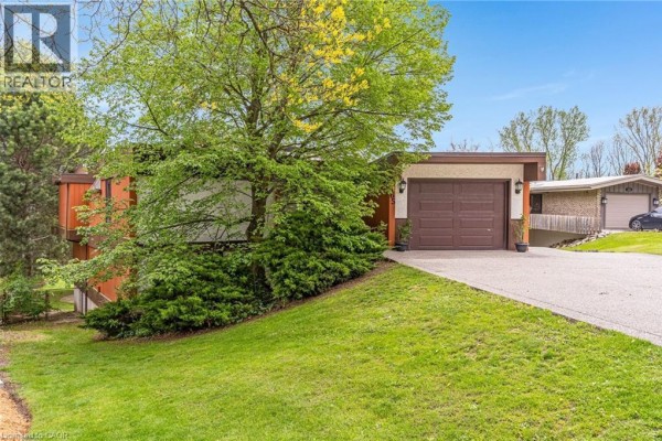 Driveway leading to a single garage door on a home with green lawn and mature trees. - 565 Fountain Street S, Cambridge