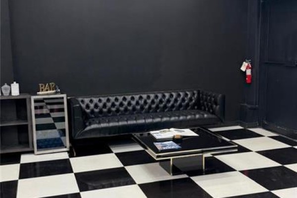 A waiting area with a tufted black leather sofa, black and white checkered floor, and a glass coffee table. - 5657 Highway 7 Unit# 4, Vaughan