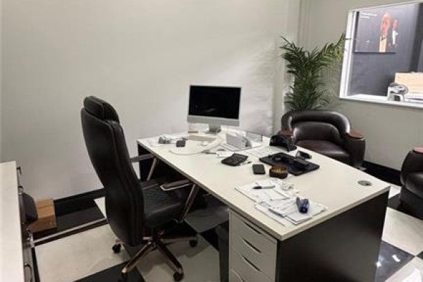 An office with a white desk, black leather chair, computer, and a plush armchair next to a potted plant. - 5657 Highway 7 Unit# 4, Vaughan