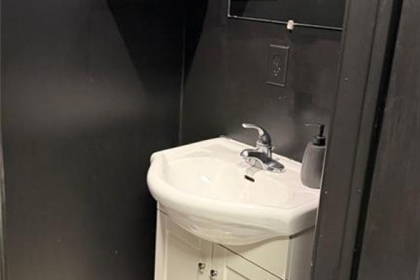 A compact washroom featuring a white pedestal sink with chrome faucet and a mirrored medicine cabinet on a dark wall. - 5657 Highway 7 Unit# 4, Vaughan