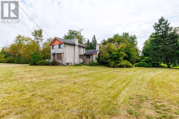 Rear exterior view of a two-story brick house surrounded by trees and dry grass. - 567 Lyons Creek Road, Welland