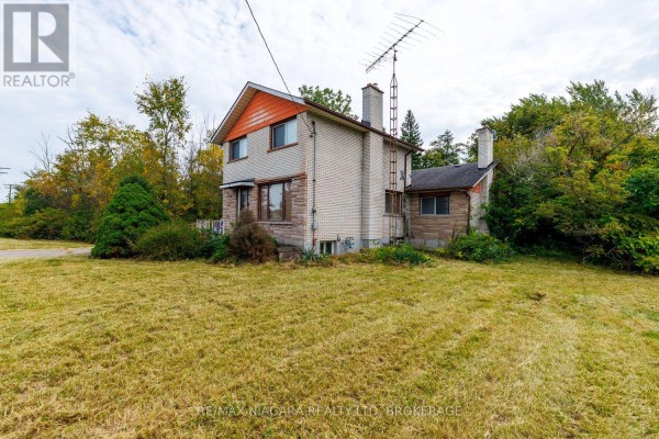 Side exterior view of a two-story brick house showing chimneys and windows, with surrounding trees. - 567 Lyons Creek Road, Welland