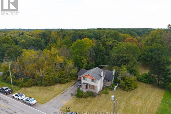 Aerial view of a two-story house with surrounding trees, a driveway, and a road with parked cars. - 567 Lyons Creek Road, Welland