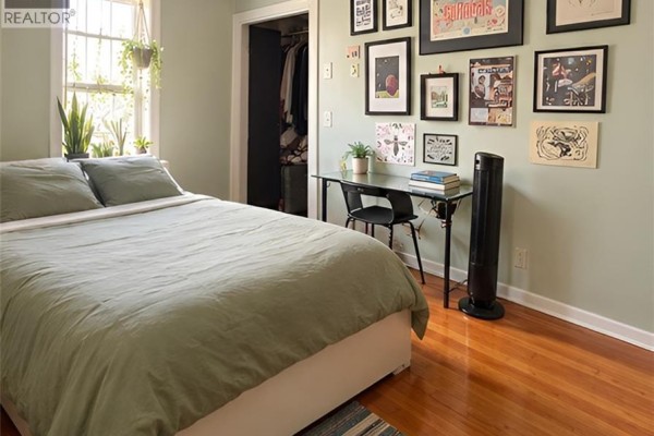 Bedroom with a bed, a desk with a chair, and artwork on a pale green wall. - 567 Woolwich Street Unit# 4, Guelph