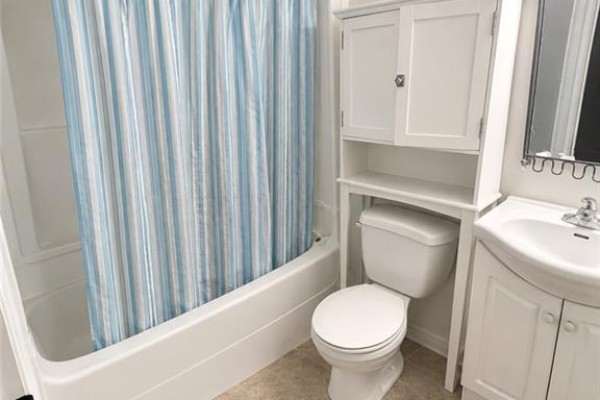 Bathroom with a white bathtub, toilet, sink, and blue and white striped shower curtain. - 567 Woolwich Street Unit# 4, Guelph