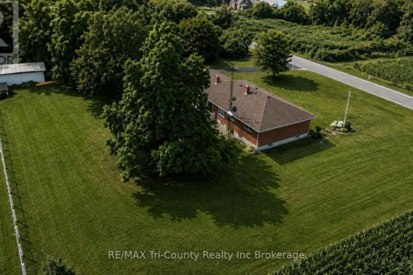 Rear exterior of a single-story brick house with a large grassy yard. - 568 7th Concession Enr Road, Norfolk