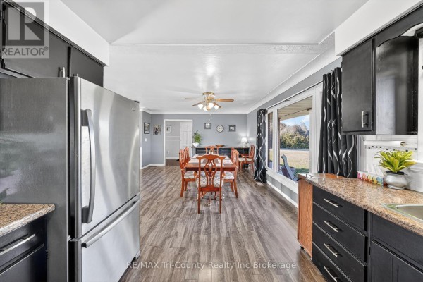 Dining area with wooden table and chairs, large window, and stainless steel fridge - 568 7th Concession Enr Road Norfolk