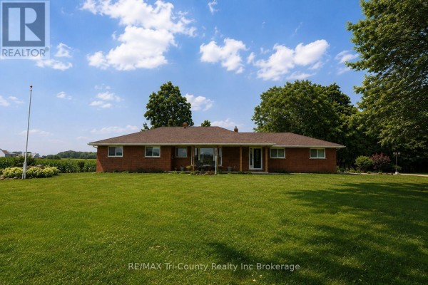 Brick patio area with two benches and a large tree in the backyard. - 568 7th Concession Enr Road, Norfolk