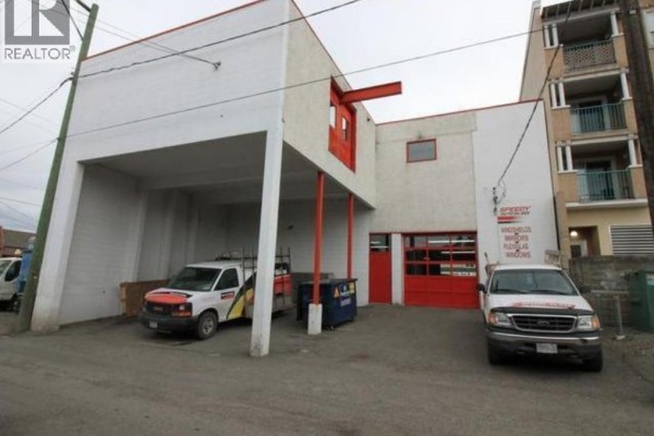 Rear exterior of commercial building with covered bays, garage doors, and service vehicles. - 568 Seymour Street, Kamloops