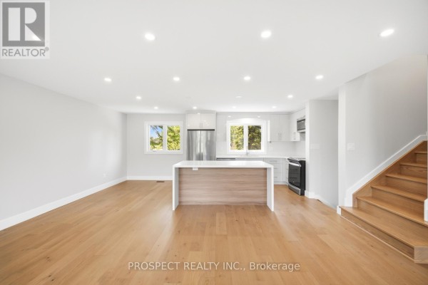 Open-concept living and kitchen area with hardwood floors, white cabinets, an island, and stairs. - 568 Simcoe Street, Collingwood