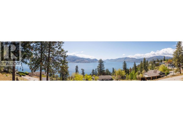 Living room with plush seating, a glass coffee table, and a large window overlooking a deck and lake. - 5687 Somerset Avenue, Peachland