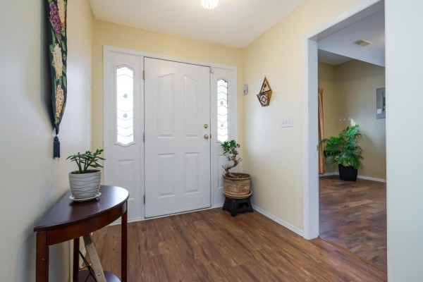 Entrance hallway with cream walls, wood-look flooring, a white front door, and a console table. - 5688 Stonehaven Street, Promontory, Chilliwack