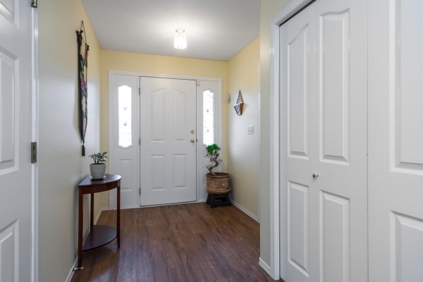 Entrance hallway with cream walls, wood-look flooring, a white front door, a console table, and a bi-fold closet. - 5688 Stonehaven Street, Promontory, Chilliwack