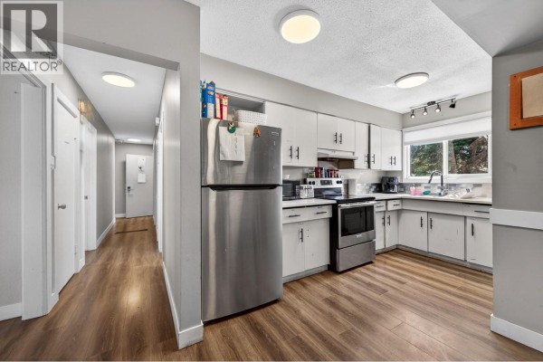 Kitchen with white cabinets, stainless steel appliances, and dark wood laminate flooring, adjacent to a hallway. - 569 Fortune Drive, Kamloops