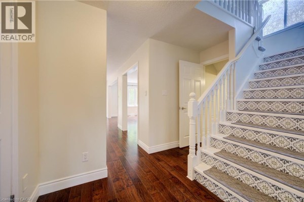 Interior hallway showing a staircase with patterned risers, dark wood floors, and doorways to other rooms. - 569 Violet Street, Waterloo