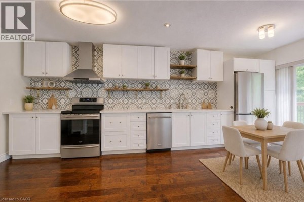 White kitchen with stainless steel appliances, patterned backsplash, open shelving, and a dining table with four chairs. - 569 Violet Street, Waterloo