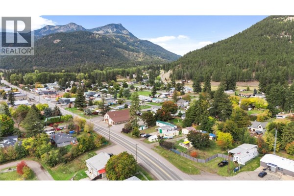 Aerial view of Falkland townsite with street, buildings, houses, and forested mountains. - 5694 97 Highway, Falkland